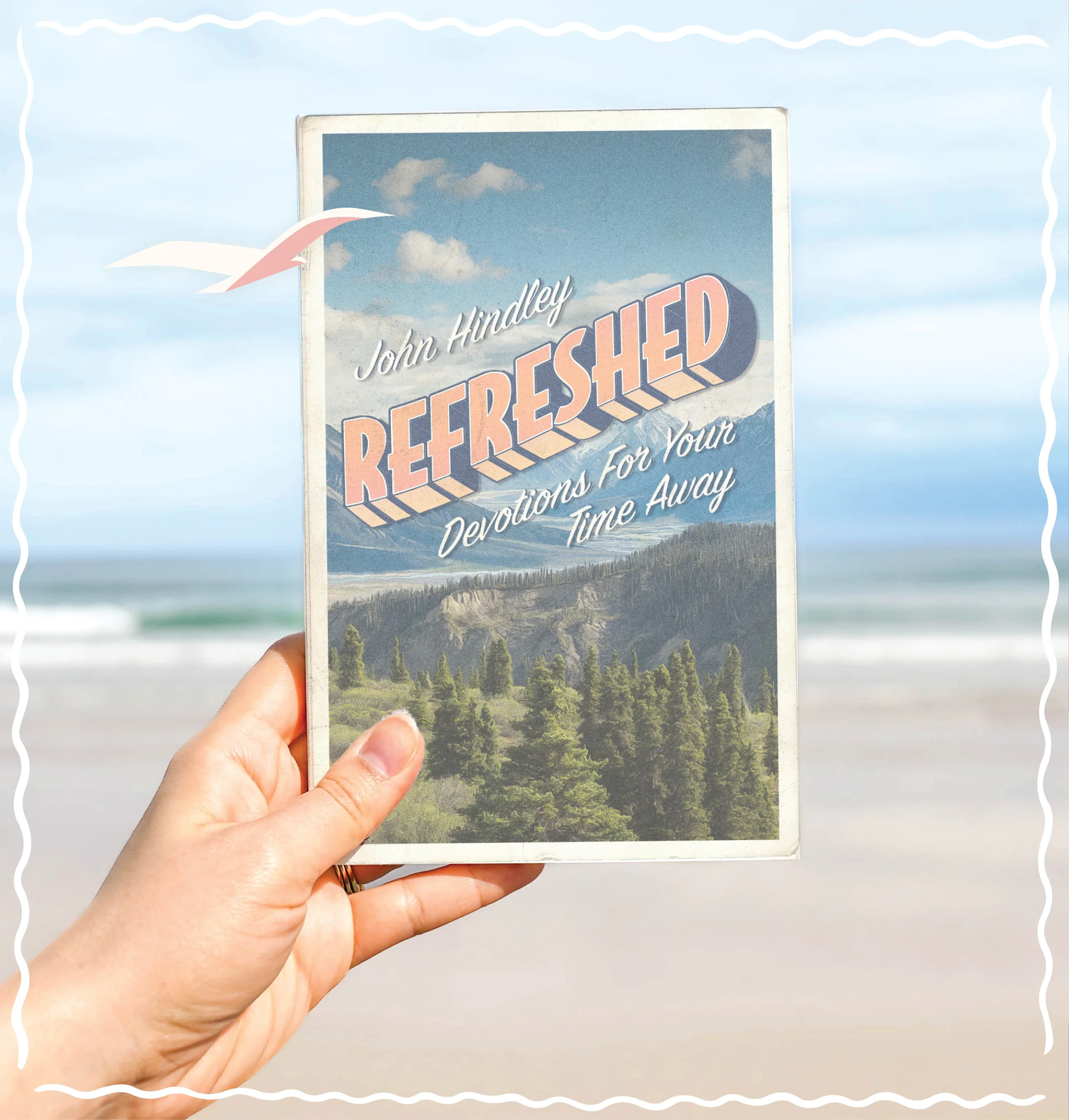 Photograph featuring a person holding up Refreshed: Devotions for Your Time Away with a beach scene in the background