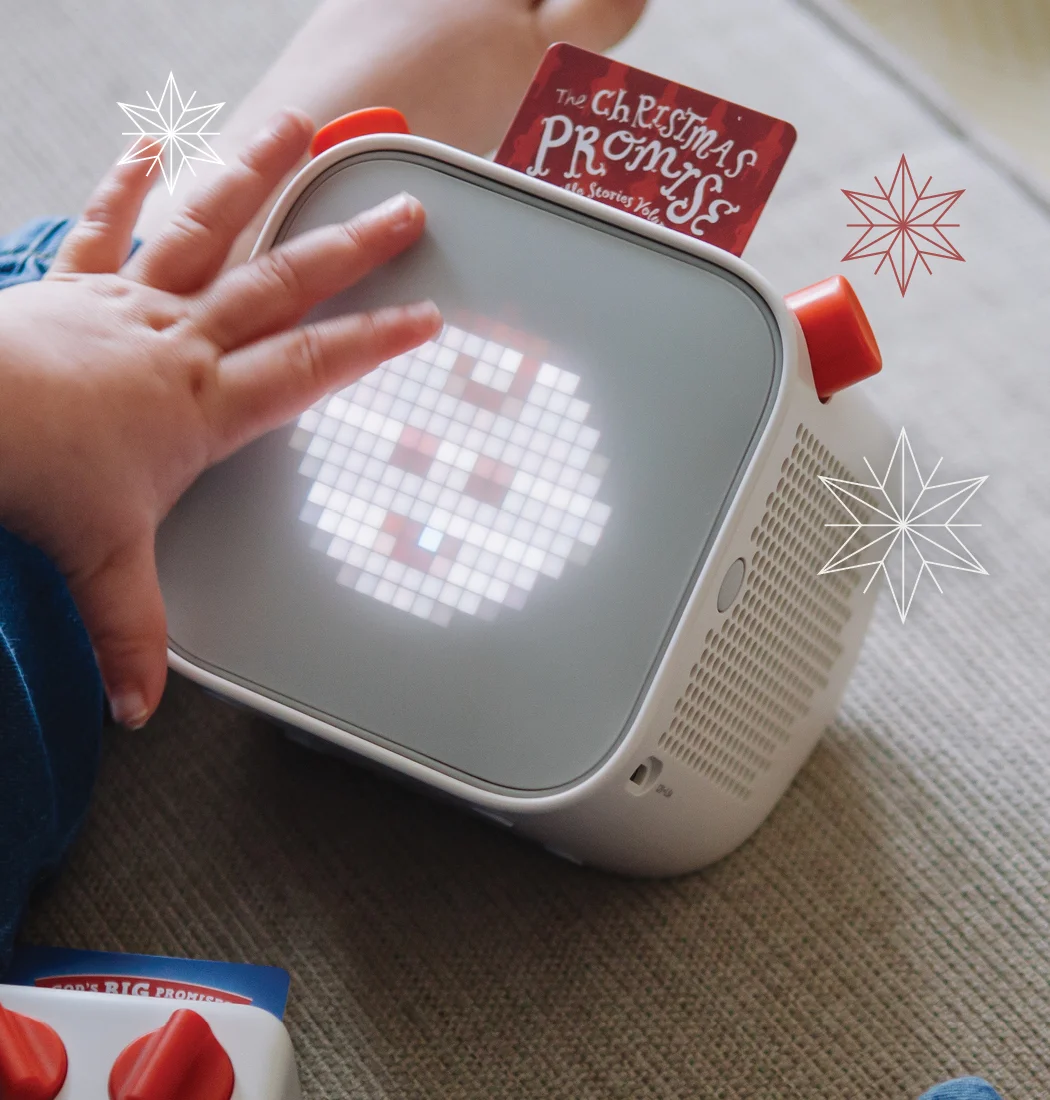 Child holding a yoto player that has a Yoto card inside with "The Christmas Promise" on it