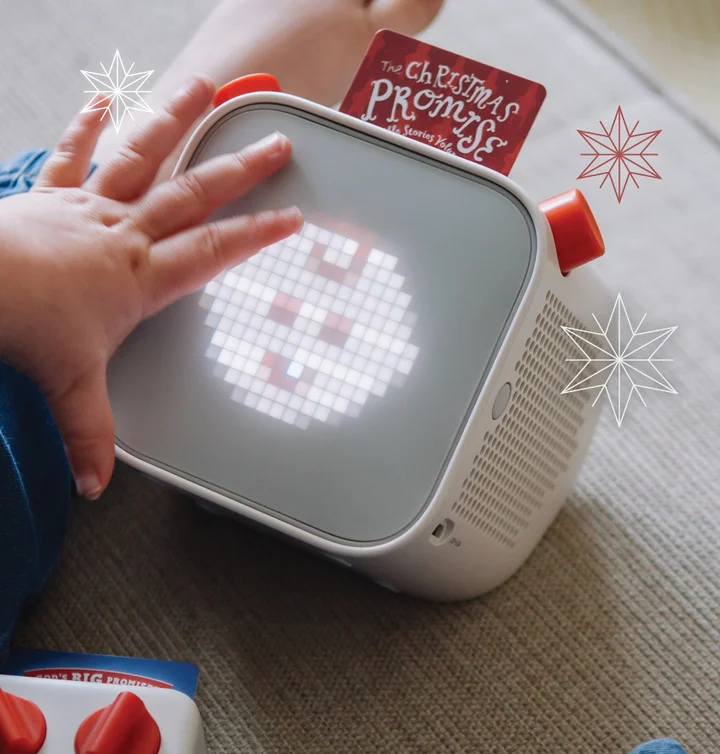 Child holding a yoto player that has a Yoto card inside with "The Christmas Promise" on it